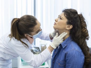 Endocrinologist examining throat of young woman in clinic. Women with thyroid gland test . Endocrinology, hormones and treatment. Inflammation of the sore throat